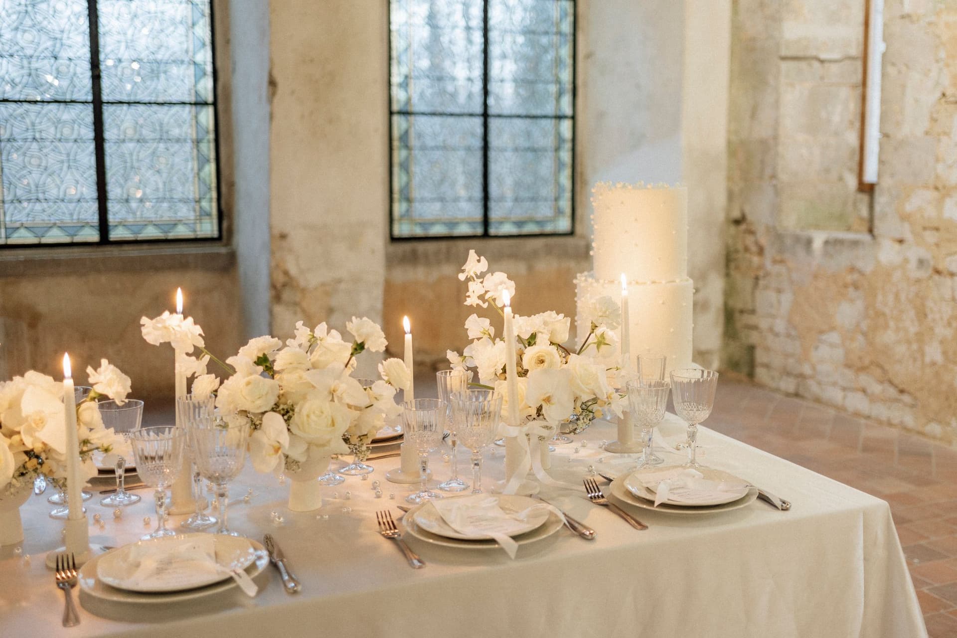Table de réception mariage en fleurs blanches, bougies et vaisselle en cristal
